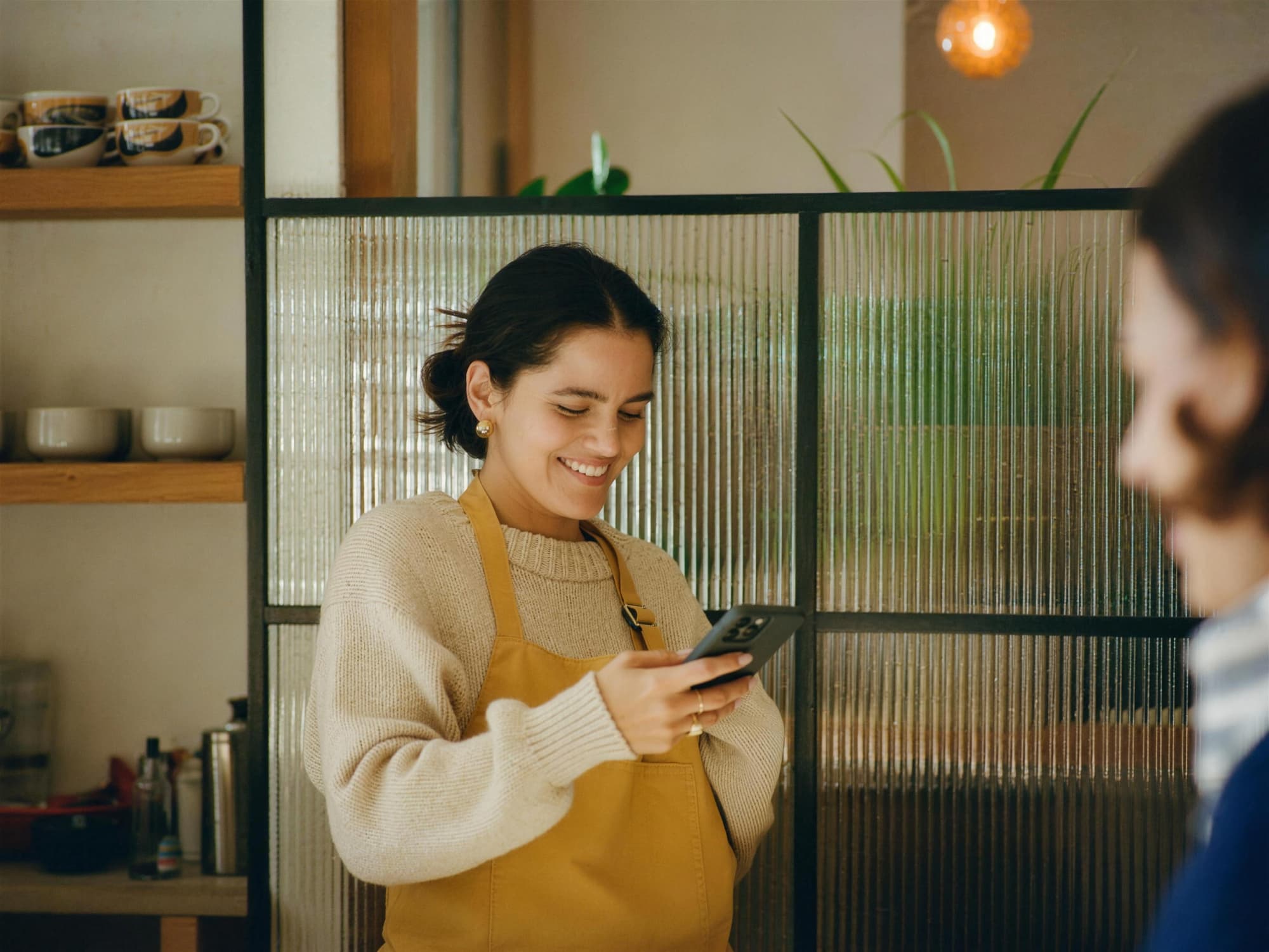 Dueña de una cafetería sonríe al revisar las respuestas de su asistente IA en su teléfono